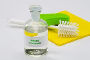A bottle of white vinegar with cleaning supplies