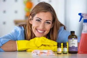 A woman in cleaning gloves stands before a selection of essential oils, prepared to utilize their natural properties for an effective clean.