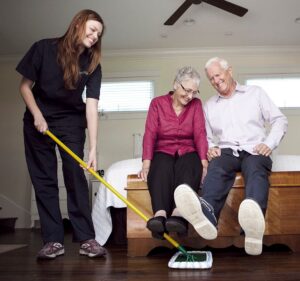 A caregiver sweeping the floor with seniors to maintain a clean and organized living environment.